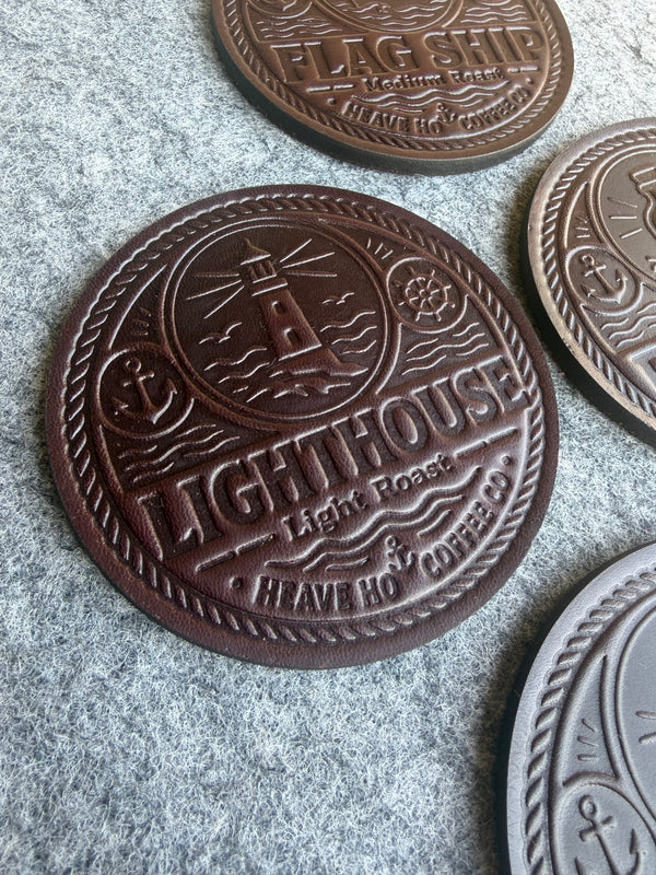 Angled close-up of embossed leather coaster showing Lighthouse artwork and leather texture